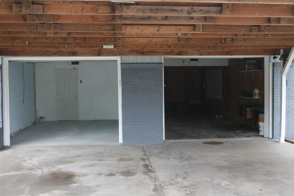 A two-car carport with an exposed wood beam ceiling, gray-painted walls, and a concrete floor.