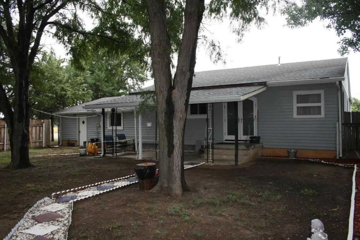 A gray house with a covered patio, a large tree, and a stone walkway in a yard.