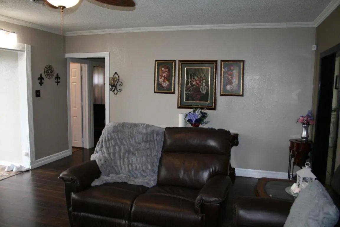 A brown leather loveseat with a grey throw blanket sits in a room with light grey walls, wall art, and hardwood floors.