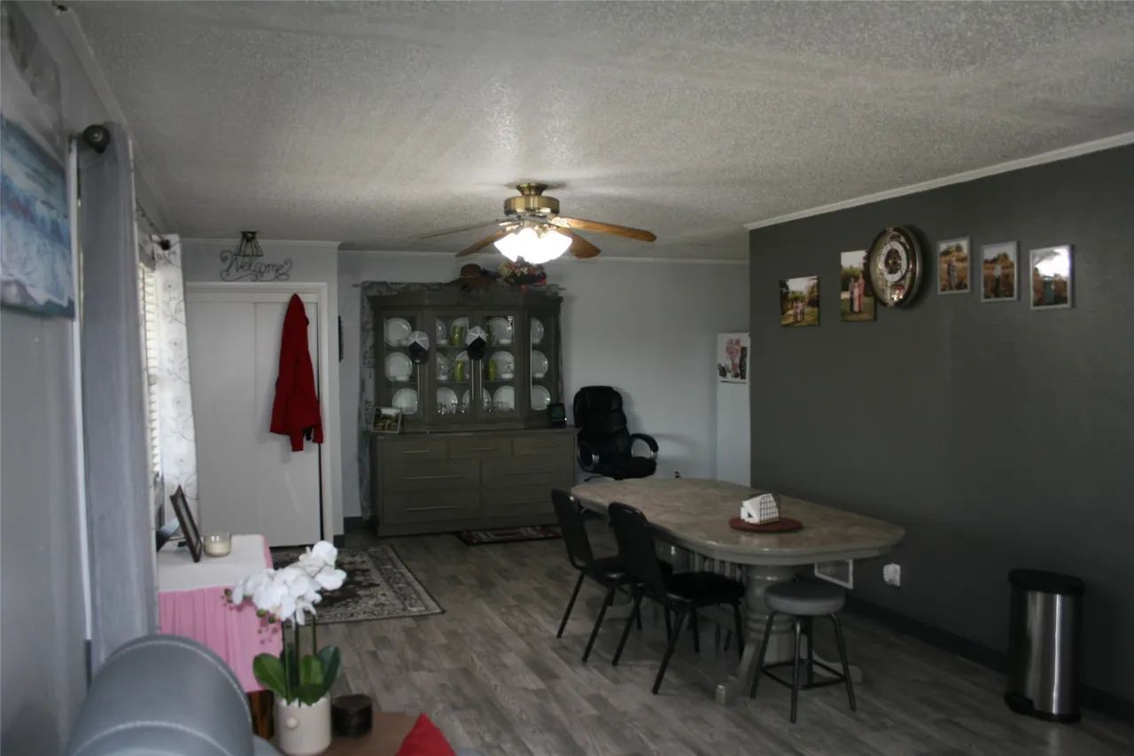 A dining area with a wood-toned table, four black chairs, a grey hutch, and a dark accent wall with framed decor.