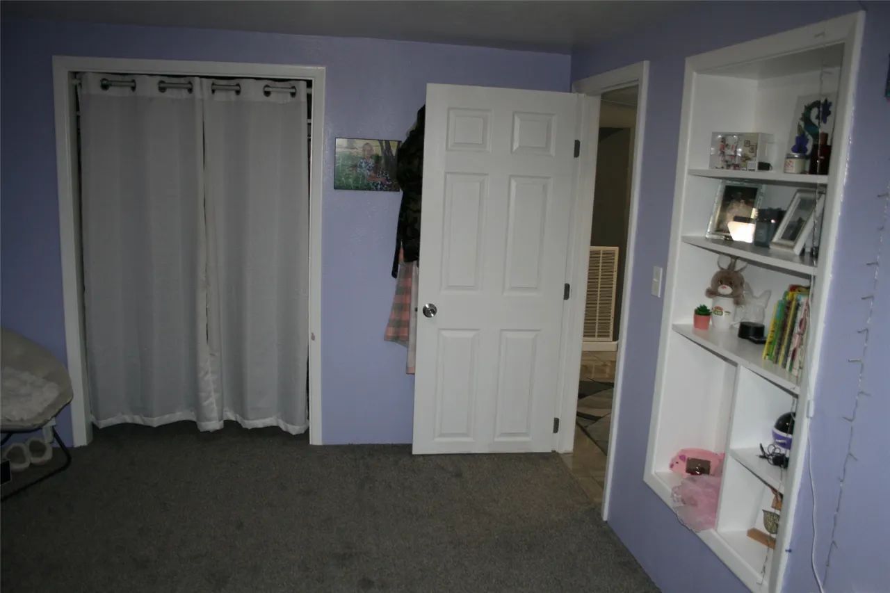 A room with light purple walls, white curtains covering a doorway, a white interior door, and a built-in display shelf.