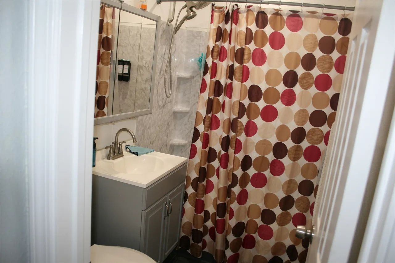 Small bathroom with a grey vanity, marble-patterned sink area, and a shower curtain featuring brown and red circles.