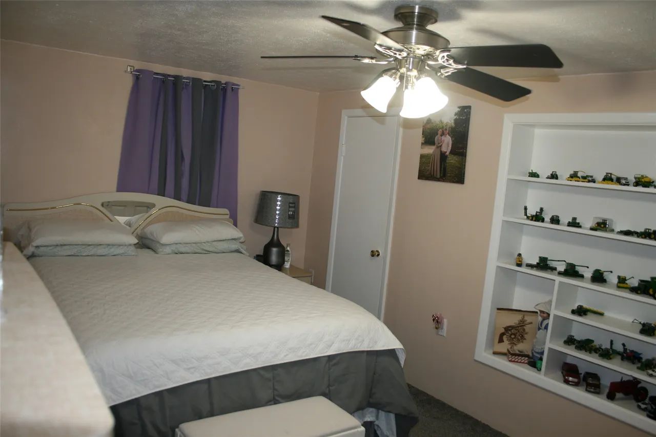 A bedroom with a bed, a ceiling fan, a purple curtain, and built-in white shelves displaying a collection of toys.