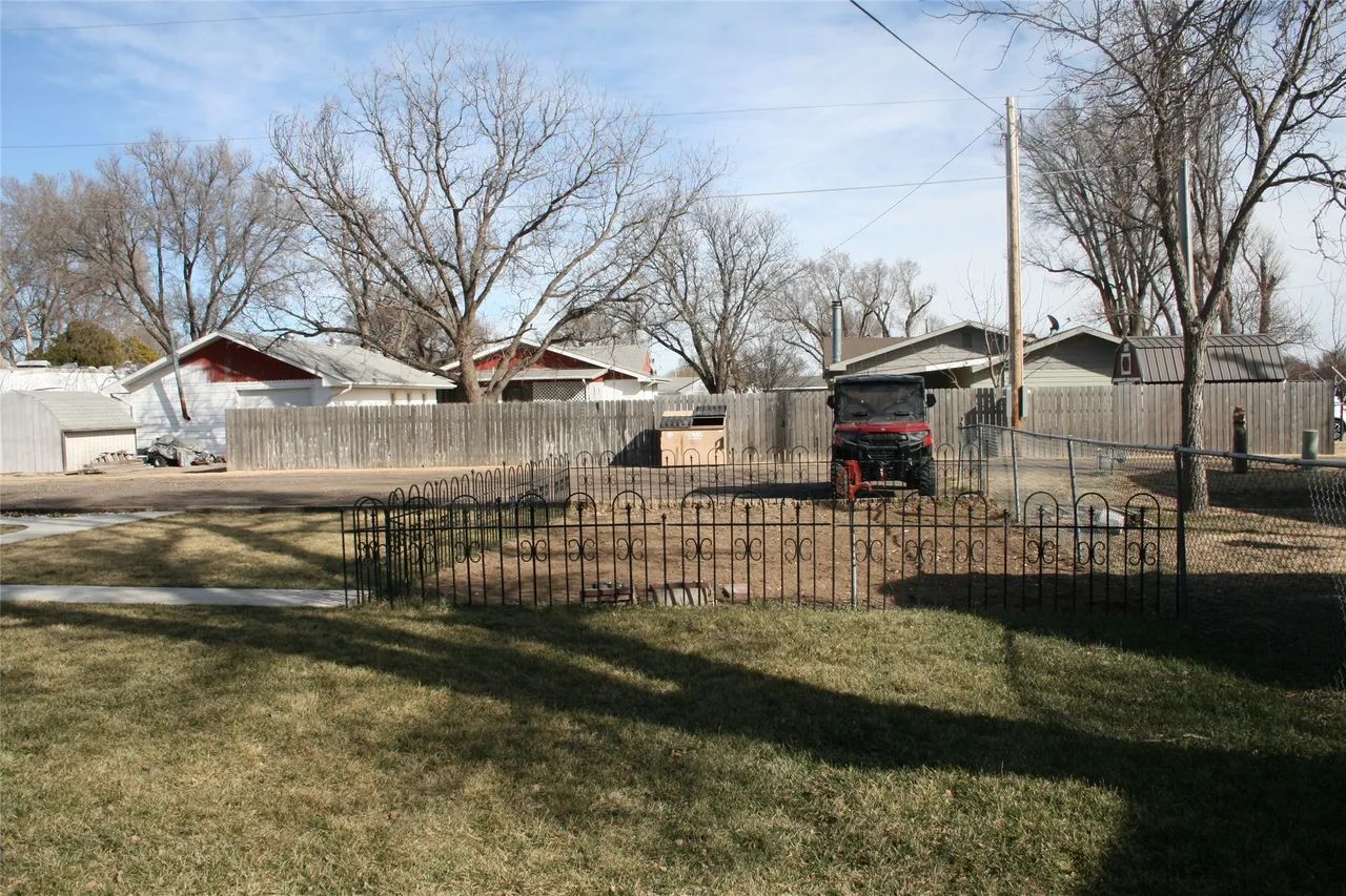 A fenced garden bed sits in a grassy backyard under a clear sky, with houses and bare trees in the background.