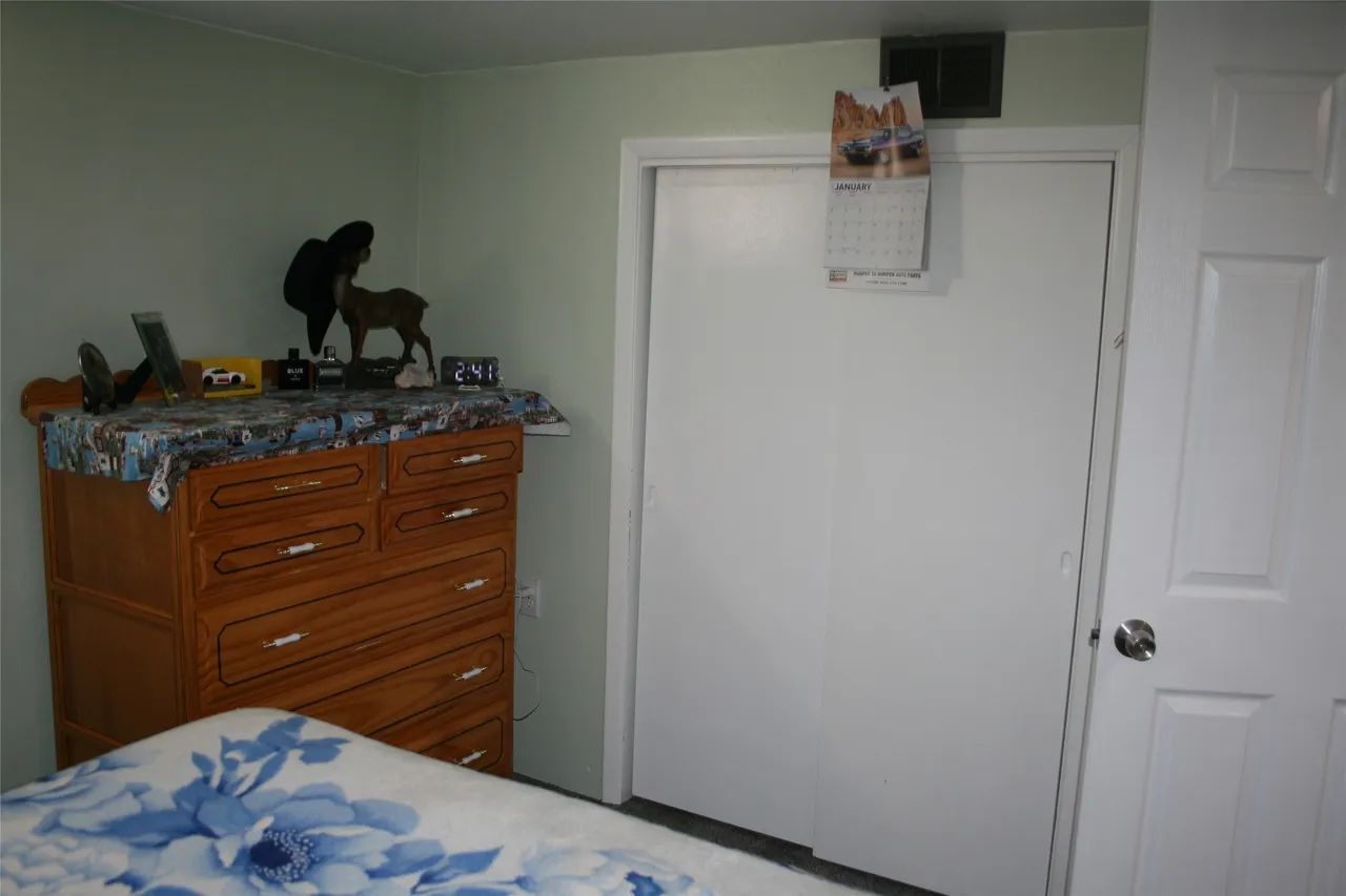 A bedroom corner featuring a wooden dresser with decorative items, a white closet door, and a floral-patterned bedspread.
