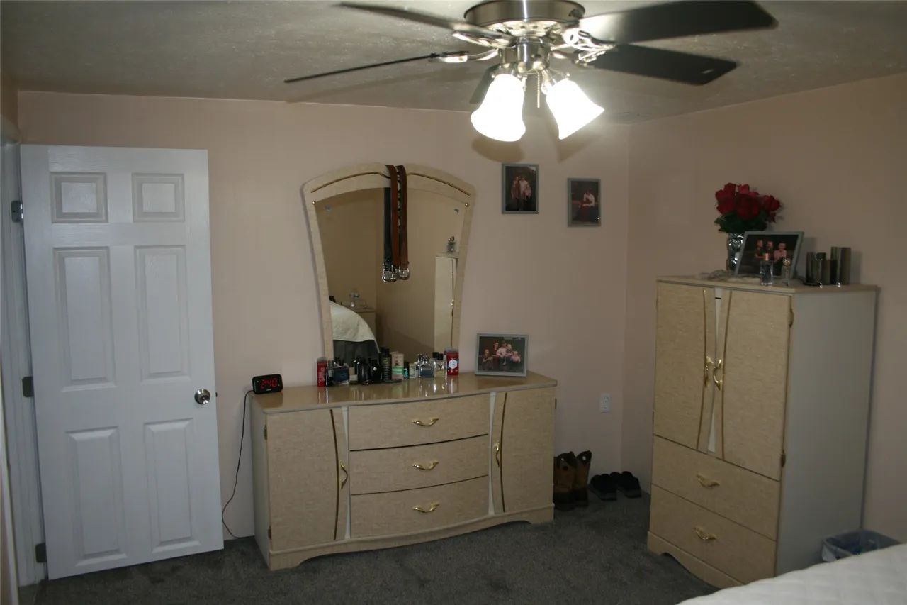 A bedroom with light pink walls, beige furniture, a ceiling fan, and a white door on grey carpet.