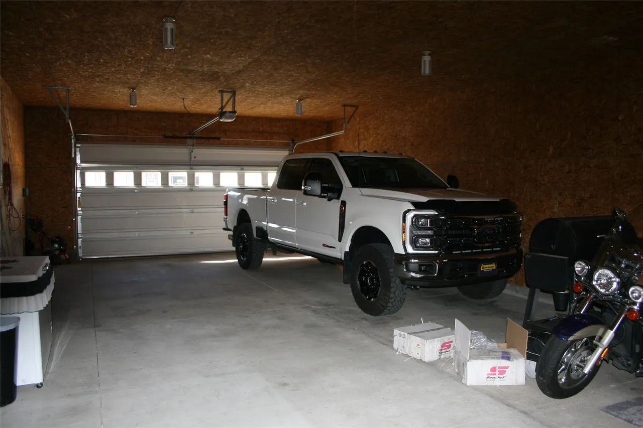 A white pickup truck and a motorcycle parked inside a spacious garage with wood-paneled walls and a concrete floor.