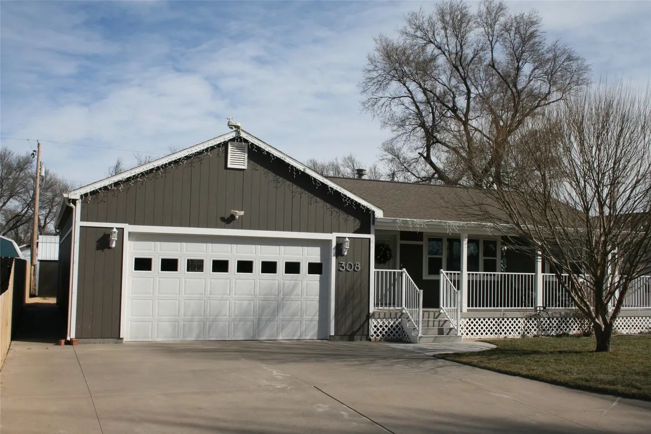 A gray, single-story house with a white garage door, a covered porch, and bare trees under a cloudy sky.
