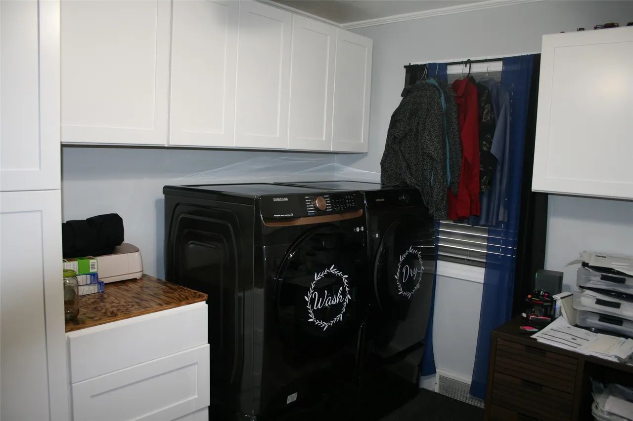 A laundry room with white cabinets, black washer and dryer, and clothing hanging on a rod against a blue curtain.