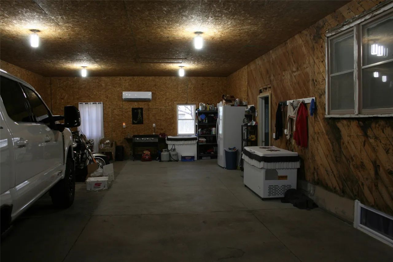 A spacious, well-lit garage with wooden walls, a white vehicle, a refrigerator, and various storage items.