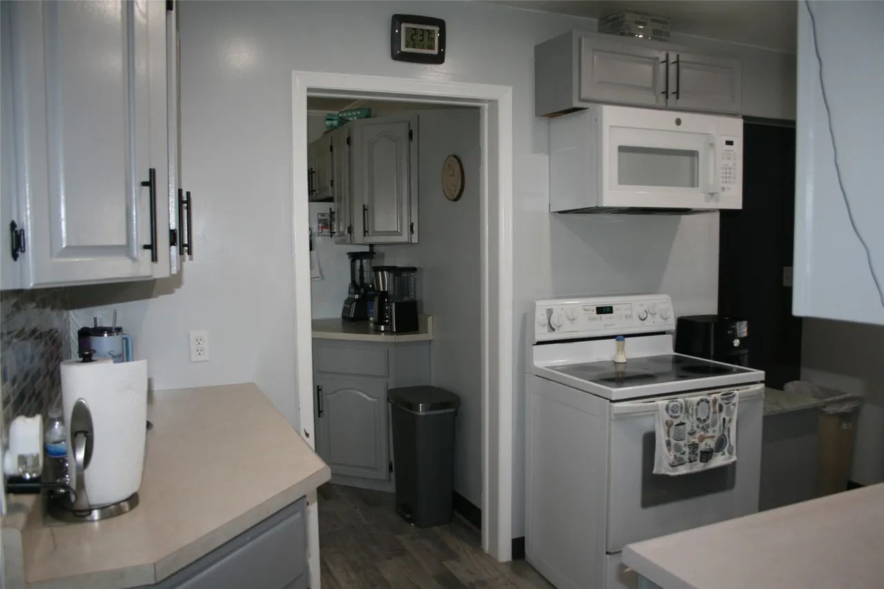 A kitchen with grey cabinets, beige countertops, a white stove, an over-the-range microwave, and a doorway to a pantry.