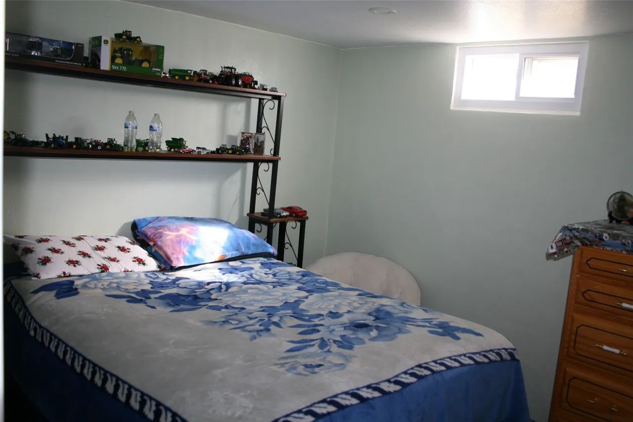 A bedroom with a bed topped with a blue and white floral comforter, a shelf with various items, and a wooden dresser.