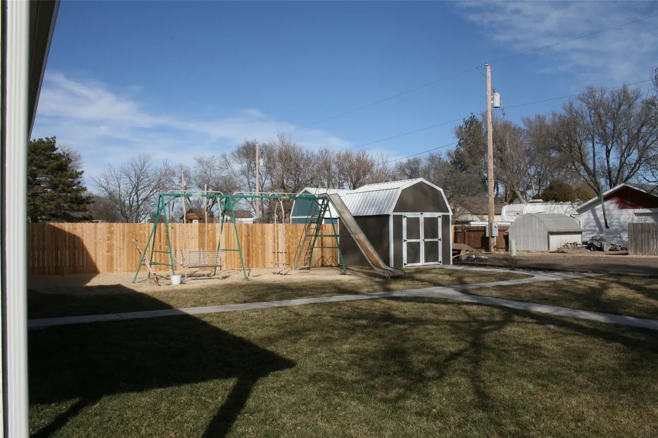 A backyard with a wooden fence, a swing set, and a small arched storage shed on a sunny, grassy lawn.