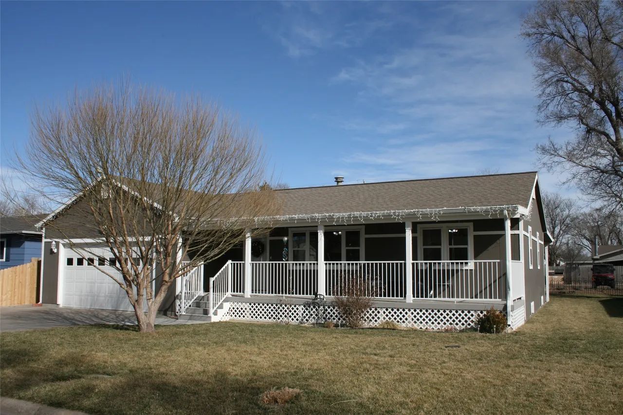A brown, single-story house with a white front porch railing and a two-car garage under a clear blue sky.