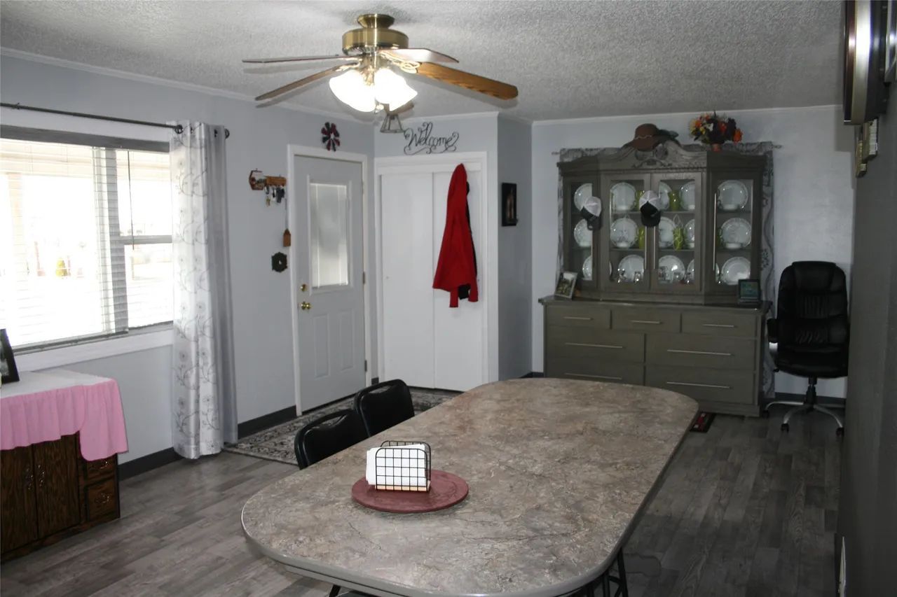 A dining room featuring a large, oval-shaped table, a grey china cabinet, a white door, and a wooden ceiling fan.