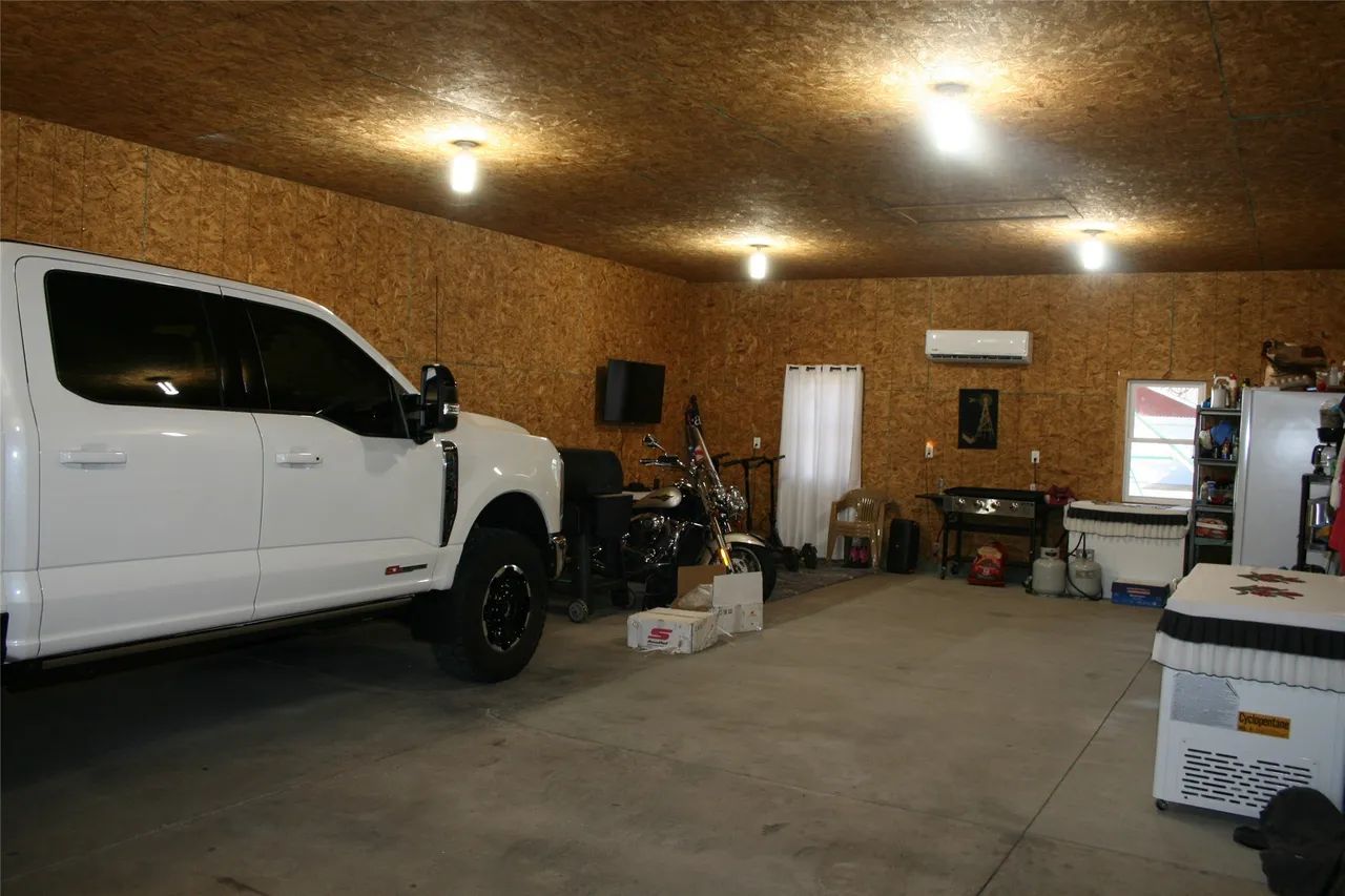 A white pickup truck parked inside a garage with OSB wood walls, a concrete floor, and overhead lighting.