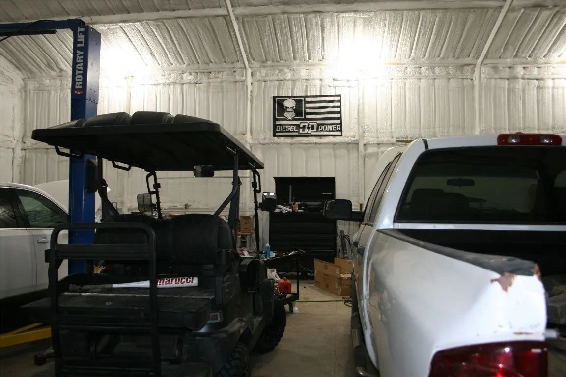 A repair shop with a side-by-side vehicle parked between a white truck and a car lift, with a wall flag in the background.