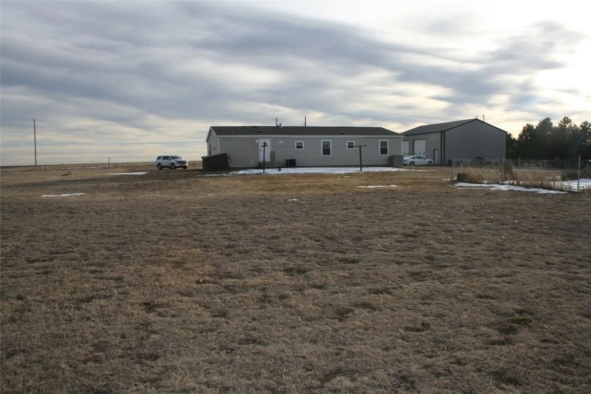 A single-story modular home with a detached garage sits on a vast, dry, brown grassy field under a cloudy, overcast sky.