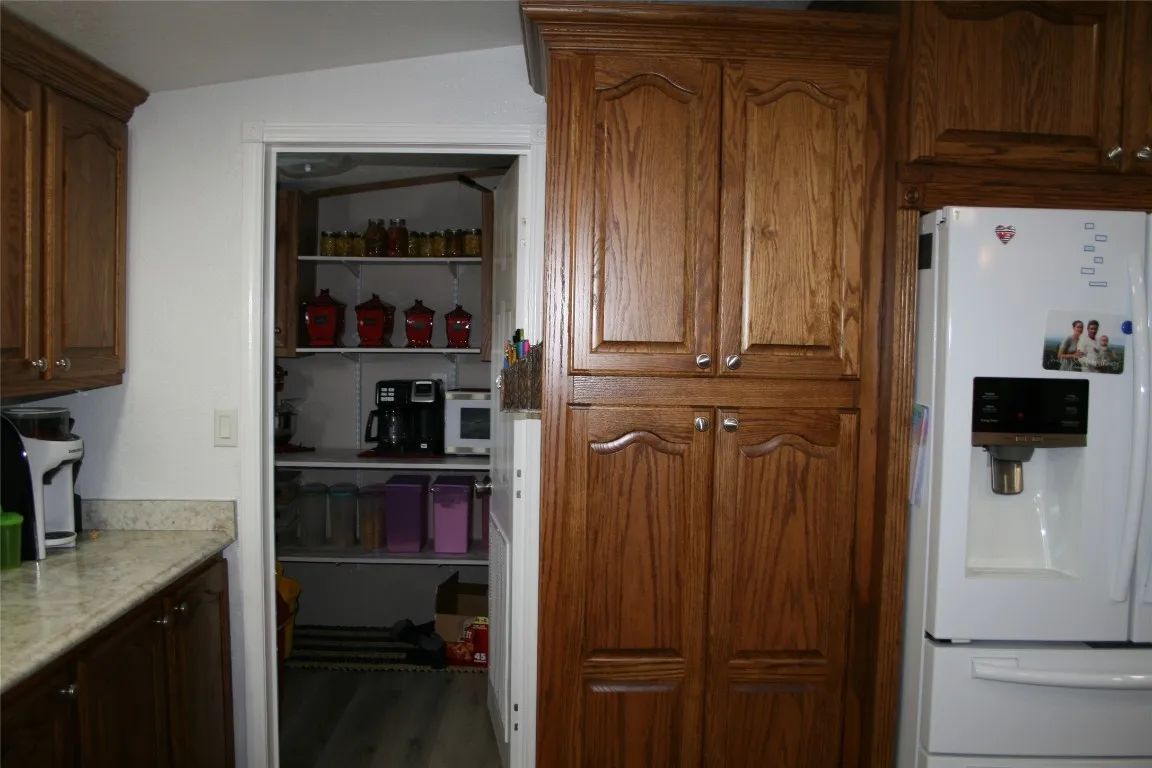 A kitchen with oak cabinets, a white refrigerator, and an open pantry door revealing shelving with kitchenware and items.