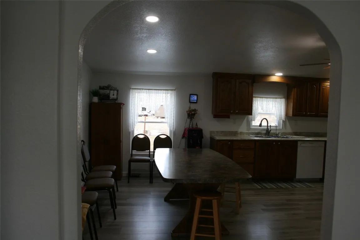 Dining area with a wooden table, chairs, and kitchen cabinetry, viewed through an arched doorway.