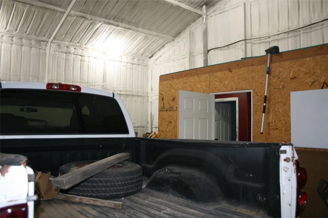 The back of a white truck parked inside a garage with spray-foam insulated walls and an interior wooden partition.