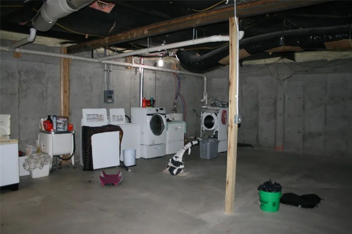 A basement laundry area with white appliances, a support post, and concrete walls and flooring.