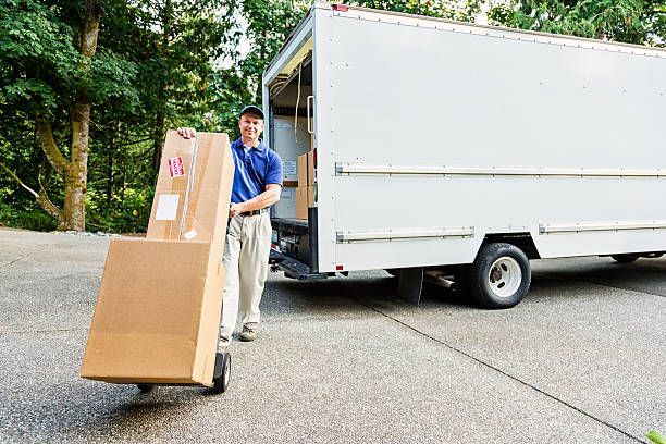 A man stands next to a moving truck, holding a box, representing licensed movers in Lakewales, FL.
