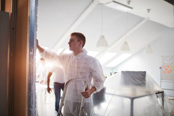 A man in a white suit applies paint to a room, signifying an office moving process.