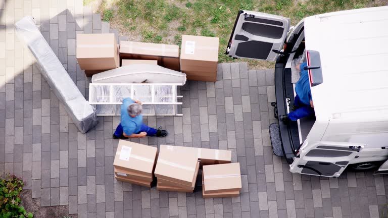 Two men in blue uniforms are moving boxes into a living room for a furniture moving company.