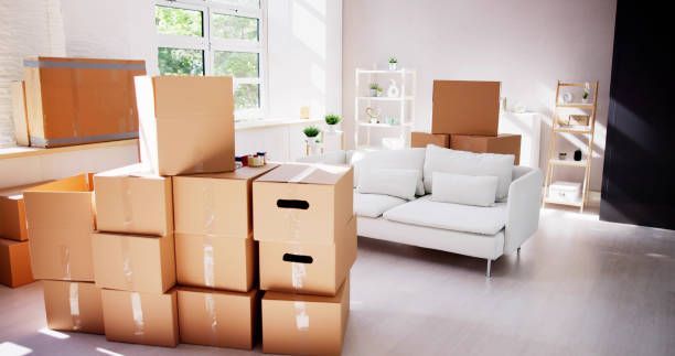 Three individuals are transporting boxes into a room, showcasing the work of a local moving company.