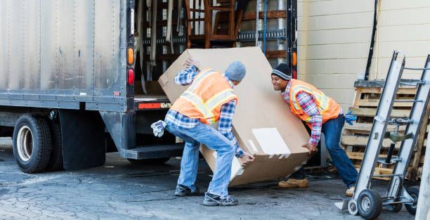 Two men unloading a large box from a truck while moving furniture to a new location.