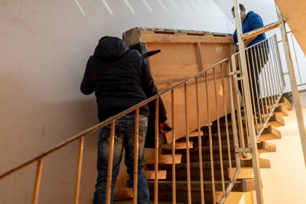 Two men are climbing a staircase, likely engaged in a furniture transfer task.