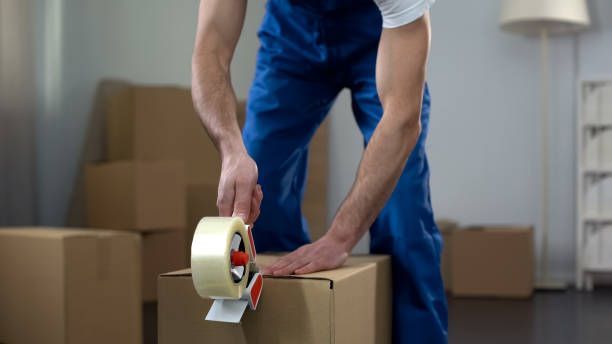 Men in blue shirts are carefully moving a large piece of furniture during a 