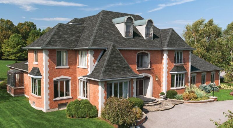 Red brick house with dark gray roof, lush green lawn, and blue sky.