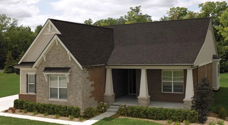 A single-story brick house with a covered porch and a dark brown roof. The house is surrounded by a green lawn and trees.