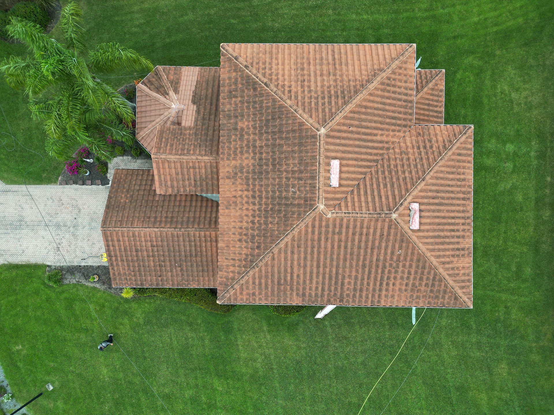 Aerial view of a house with a brown roof, driveway, and green lawn.