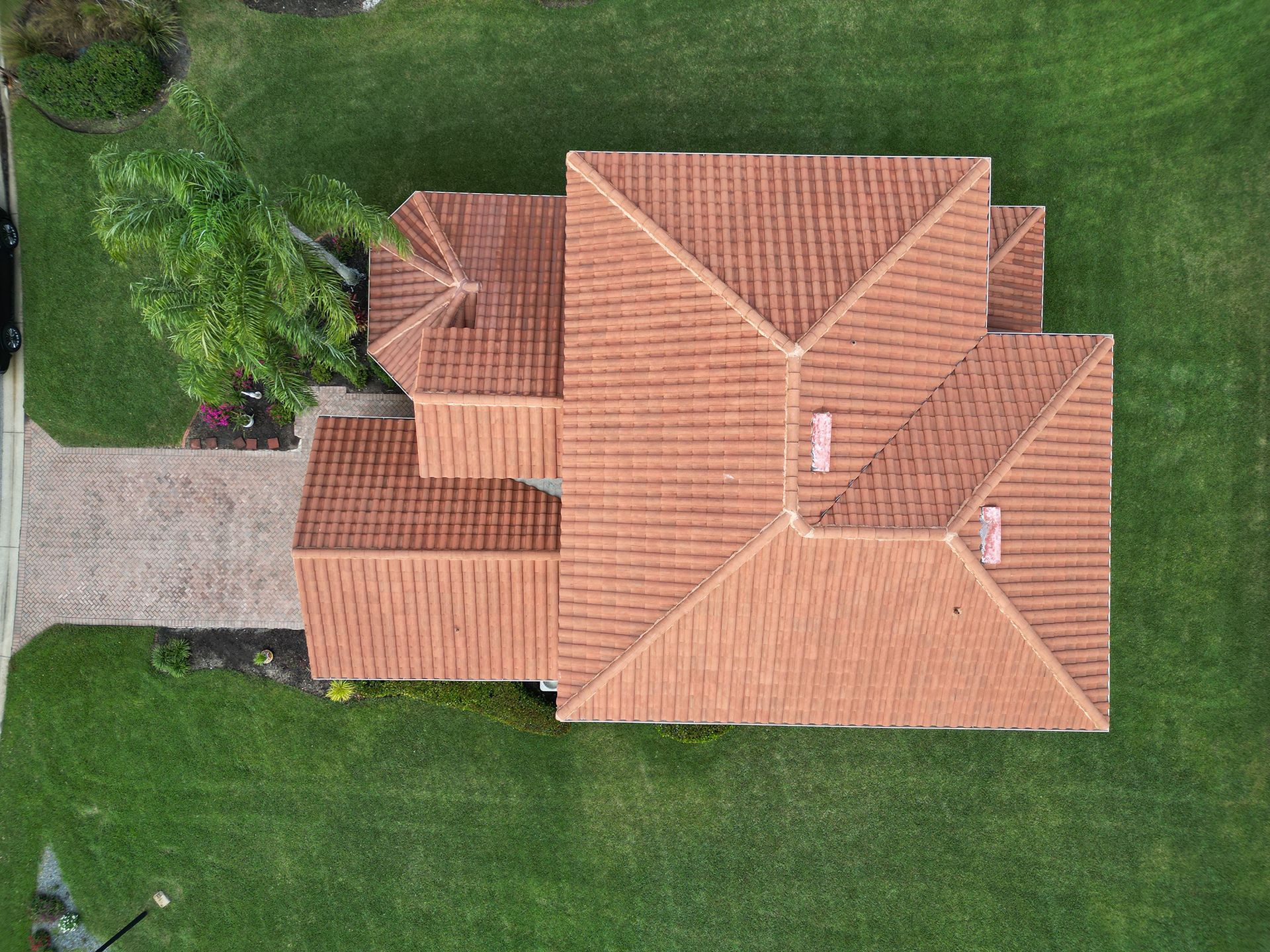 Aerial view of a house with a brown tile roof, driveway, and green lawn.