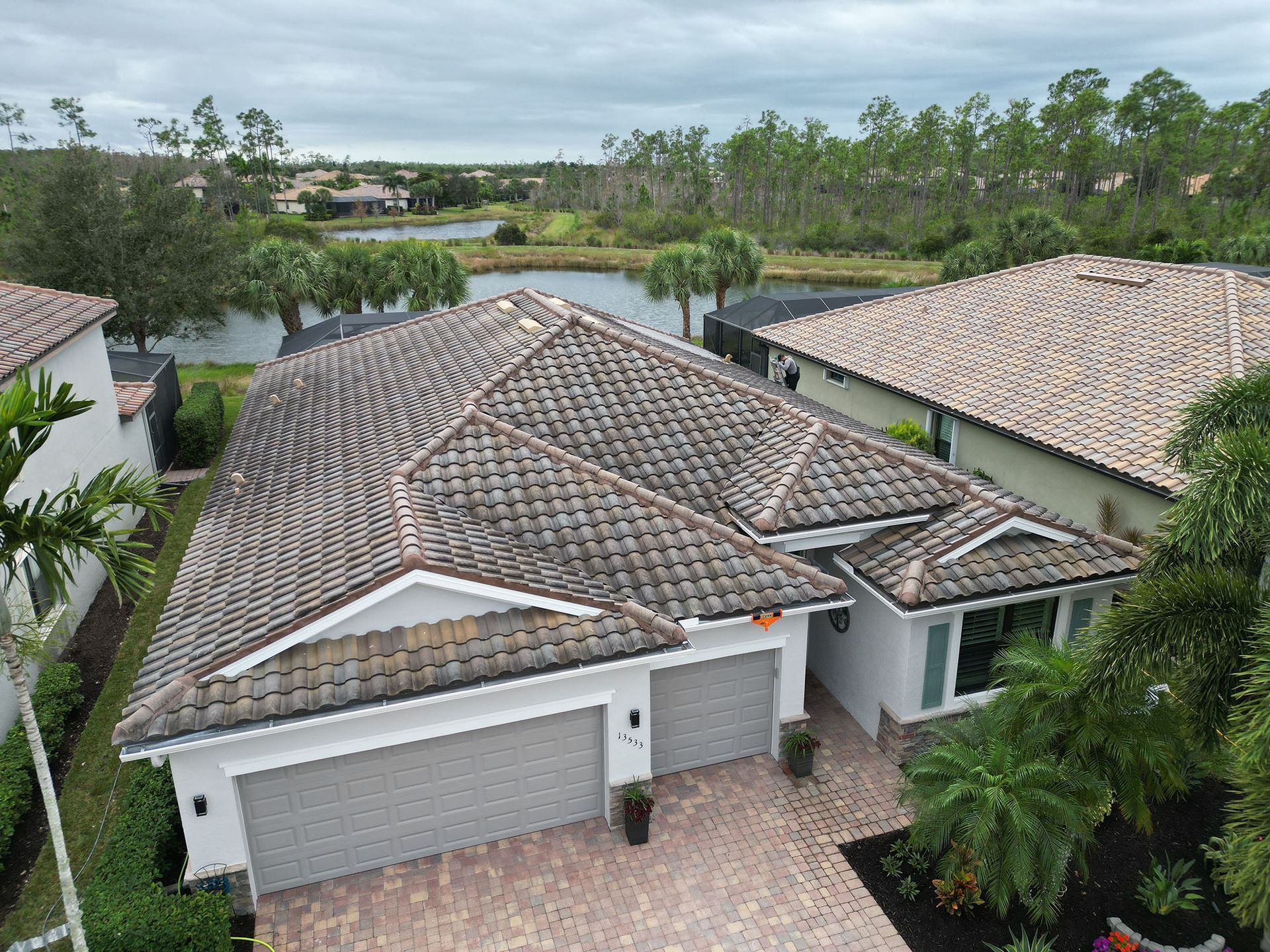 Aerial view of a house with a tiled roof, garage, and lush greenery near a waterway.