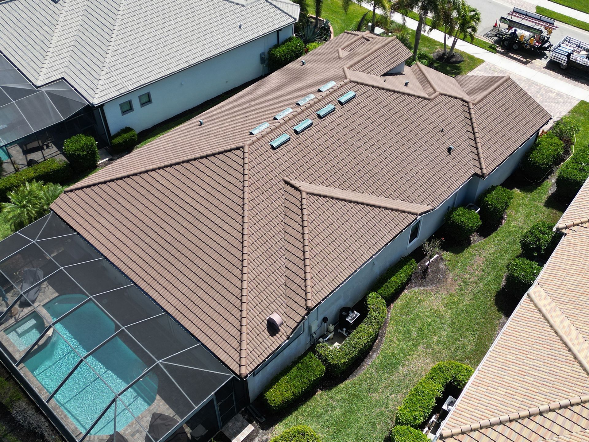 Aerial view of a tan-roofed house with a screened pool enclosure and green yard.