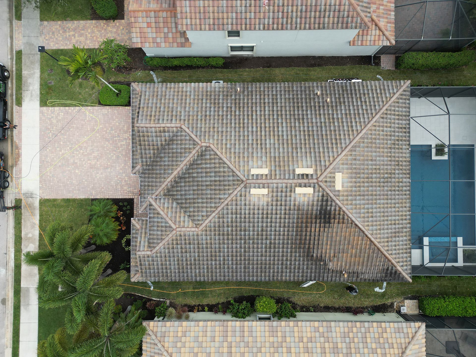 Aerial view of a house with a tiled roof beside a swimming pool and palm trees.