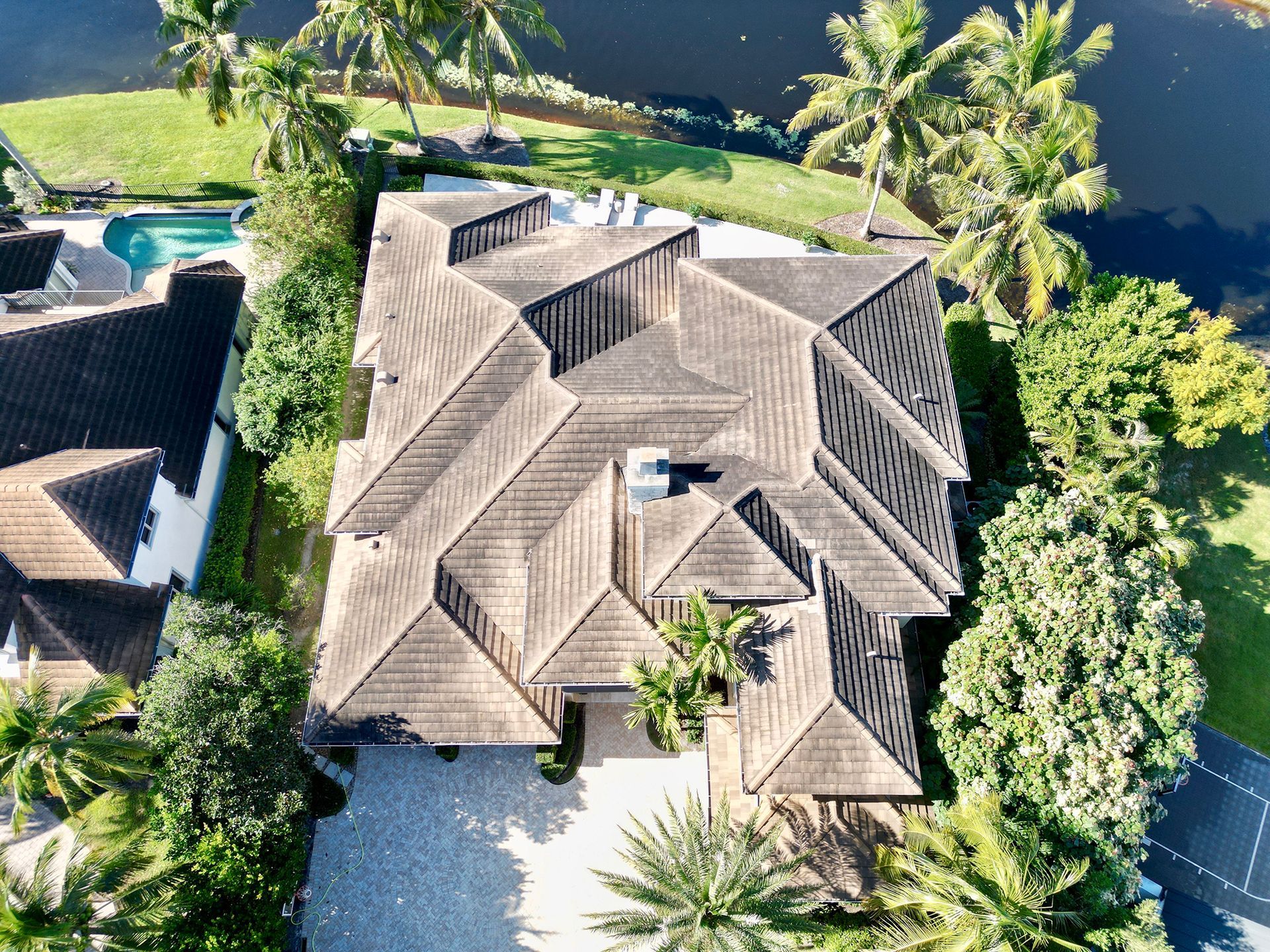 Aerial view of a tan-roofed house surrounded by palm trees near the water