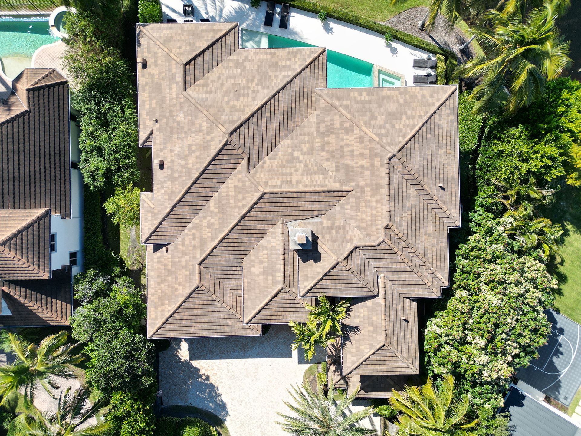 Aerial view of a tan-roofed house surrounded by lush green trees and a turquoise pool
