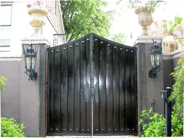 Black, arched wooden gate with vertical planks, flanked by brick pillars with urns and lanterns.