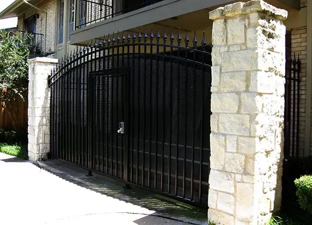 Black metal gate between stone pillars, entrance to a building.
