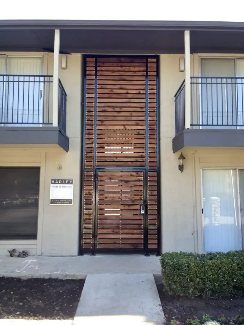 Wooden slat wall and door on a building facade, with metal accents, flanked by balconies and windows.