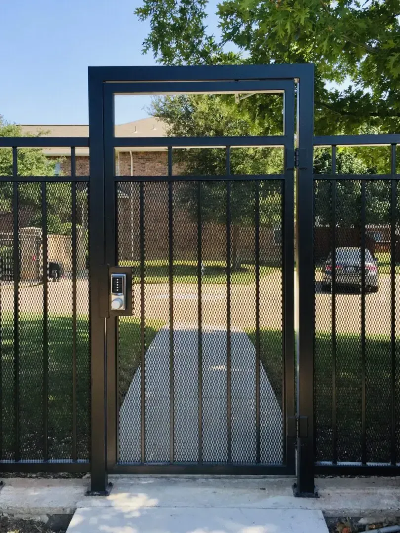 Black metal gate with diamond mesh panel and call box, set in concrete walkway.