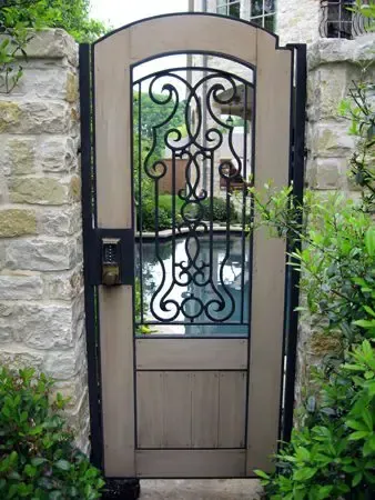 A decorative wooden gate with wrought iron detail set in a stone wall, leading to a garden.