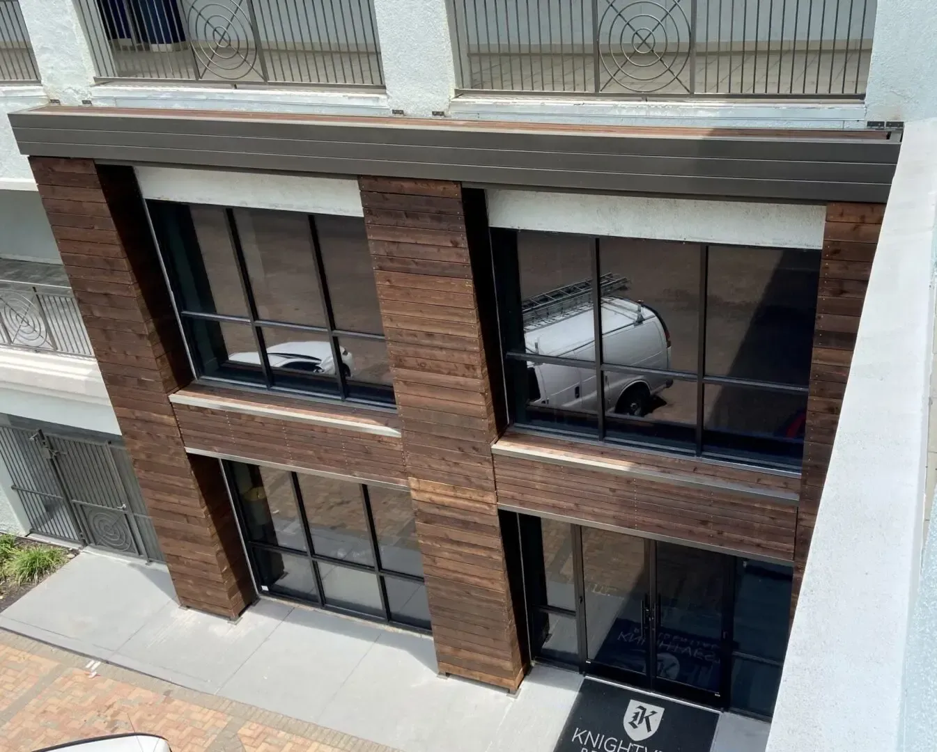 Building facade with brick columns, large windows reflecting a car, and an awning.