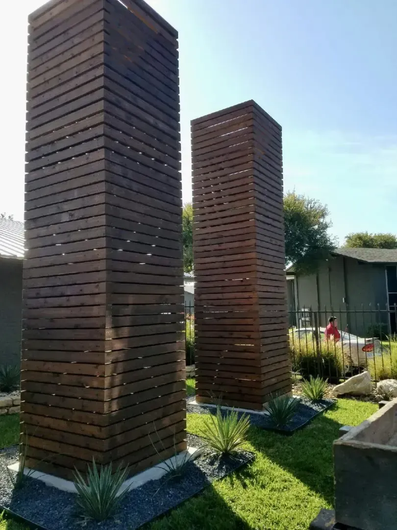 Two tall wooden structures in a landscaped yard with green grass and blue sky.
