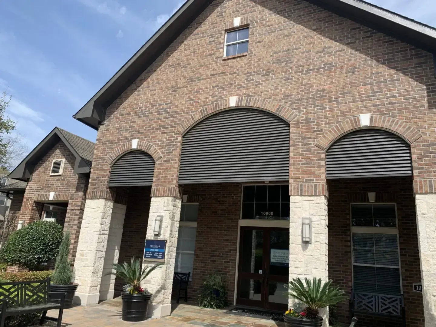 Brick building with arched entrances, awnings, and decorative plants.